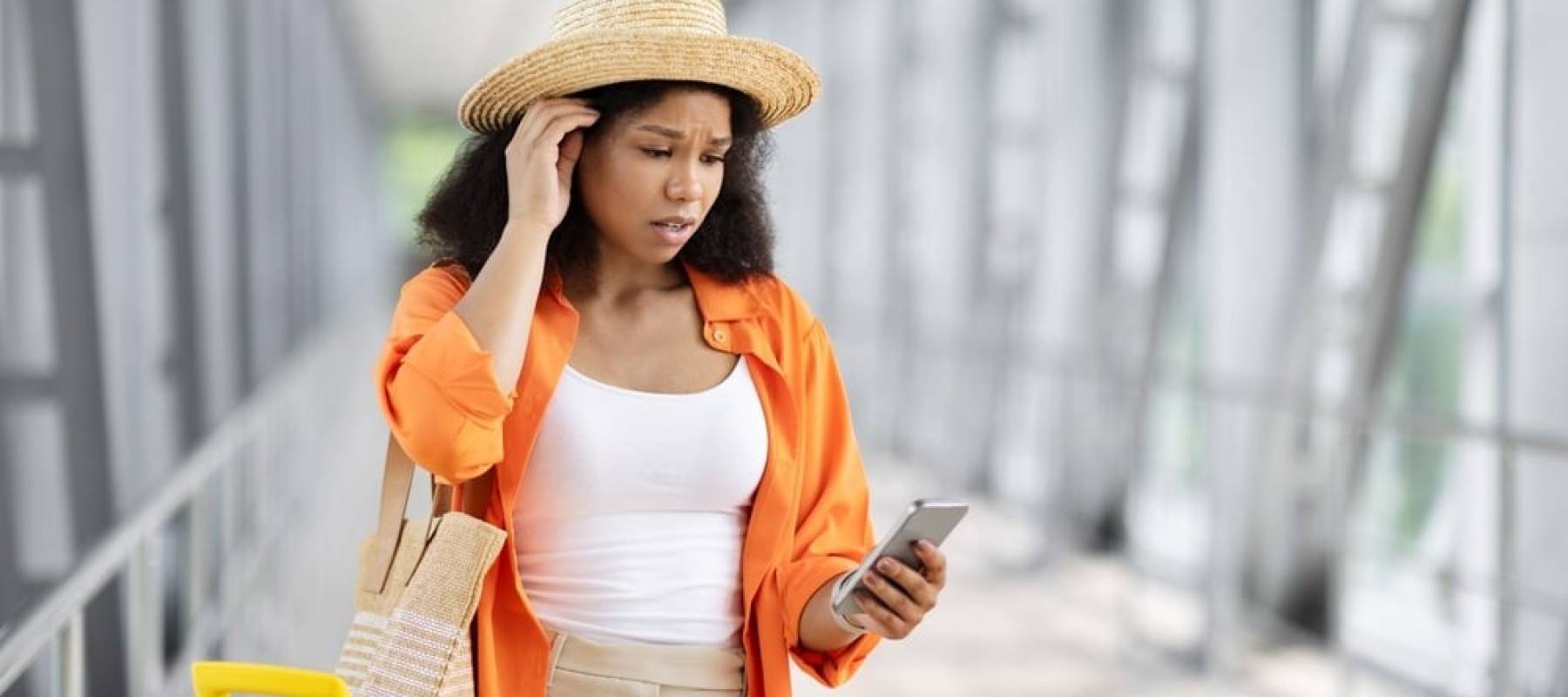 A young Black woman in an airport, looking at her phone with concern