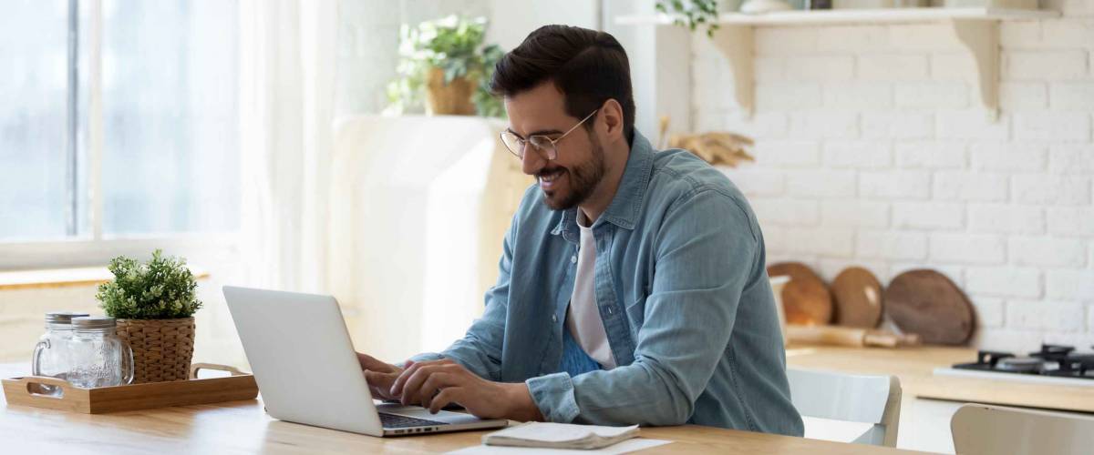 Smiling young man working on laptop in modern kitchen.