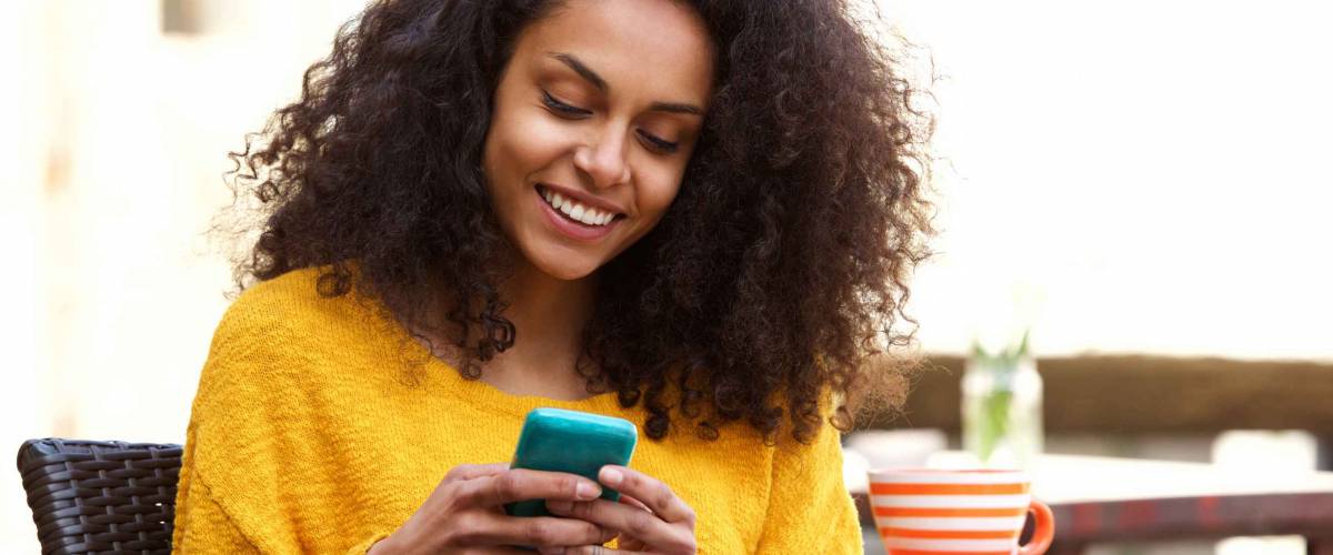 Close up portrait of beautiful young african american woman reading text message on mobile phone at coffee shop
