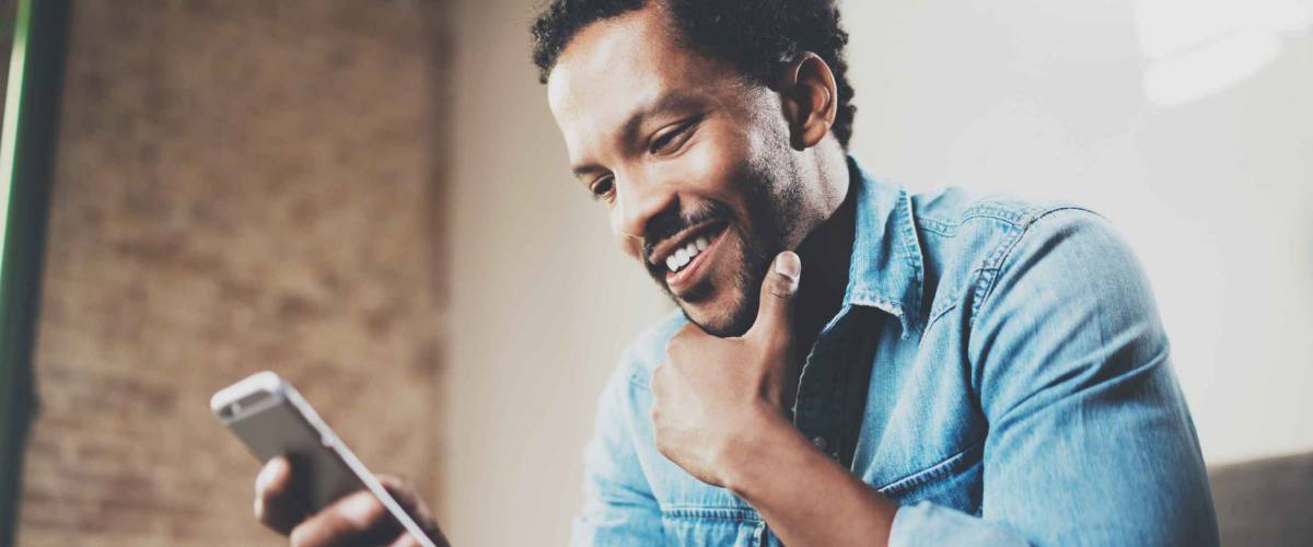 Happy bearded African businessman using phone while sitting on sofa at his modern home.Concept of young people working mobile devices.Blurred background