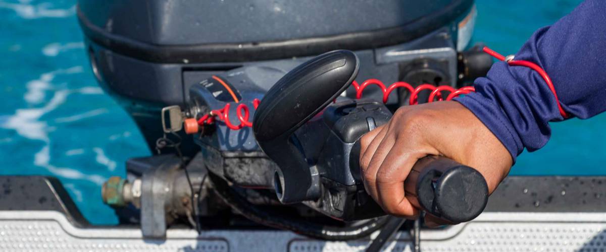 Male hand driving a inflatable boat holding the tiller of an outboard motorboat, close up, outdoors.