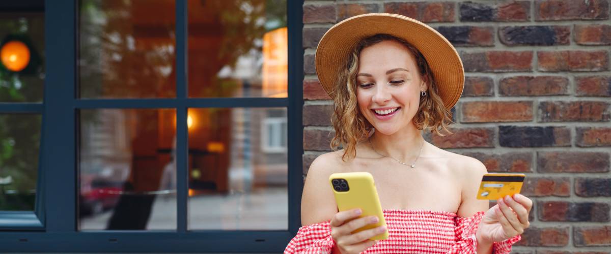 Young satisfied happy woman 20s wear pink dress hat using mobile cell phone credit bank card