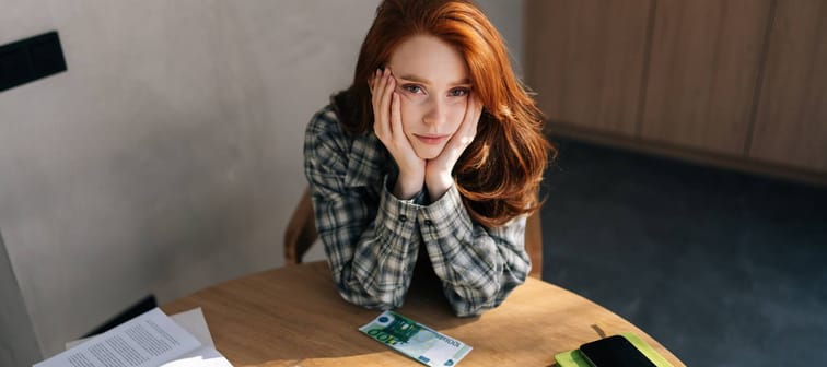 Young woman sitting at a table with money and bills looking worried