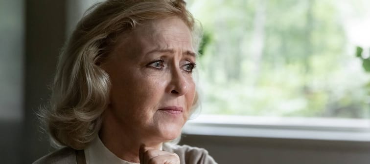 An older woman ponders by a window.