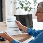 Mature woman reviewing expenses and using a calculator to cut costs