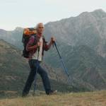 An older couple hike across a rise with mountains in the distance.