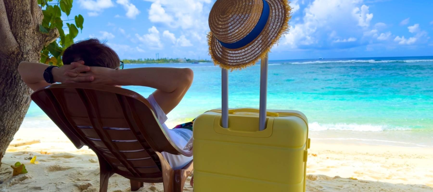 Traveller relaxing on the beach with suitcase beside the chair (enjoying travel perks)