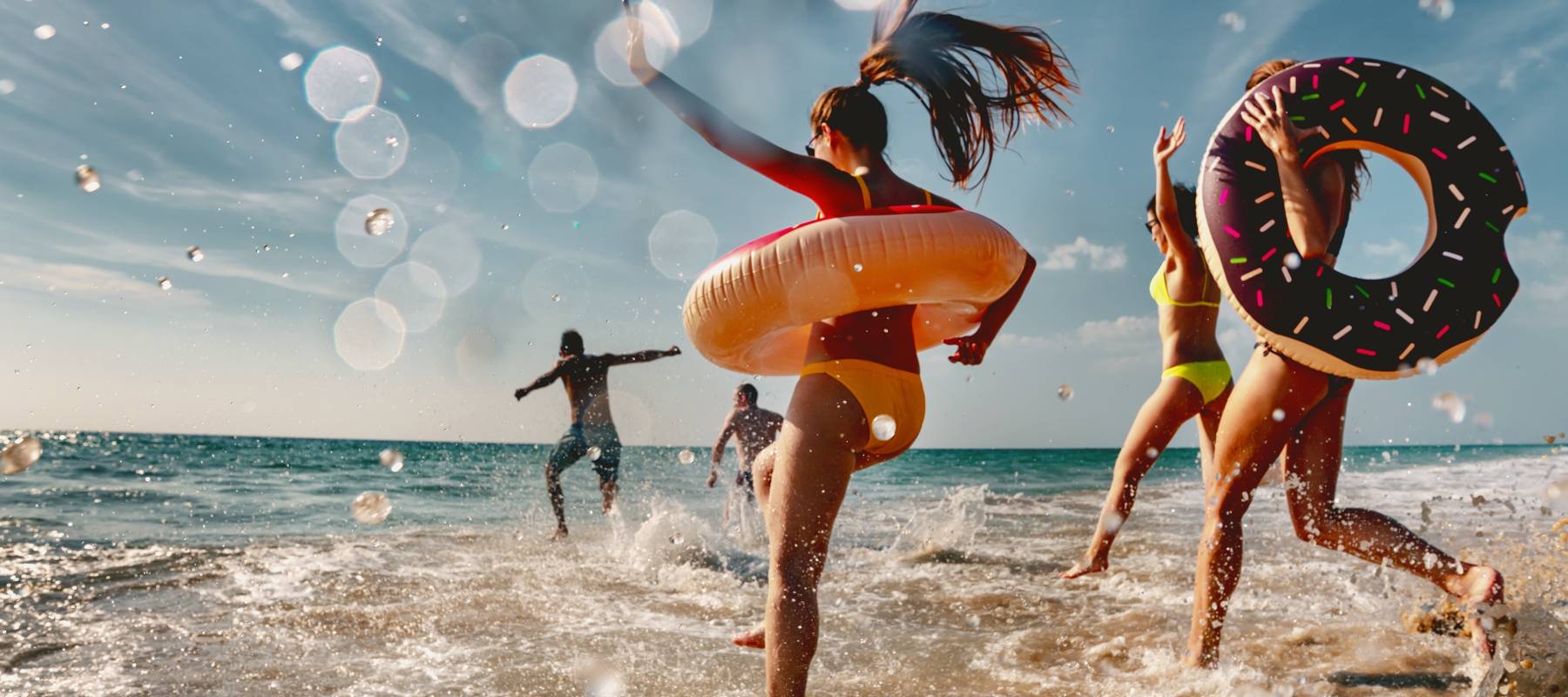 Group of friends are having fun and running to sea beach with inflatable donuts