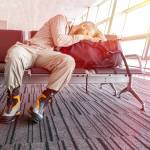 Cancelled flight. Man sleeping on his travel luggage inside airport terminal.