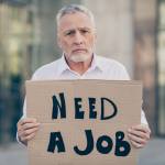 Older man holds up "Need a job" sign
