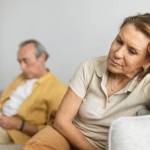 Woman looking disappointed and bothered on couch while man using smartphone in background.