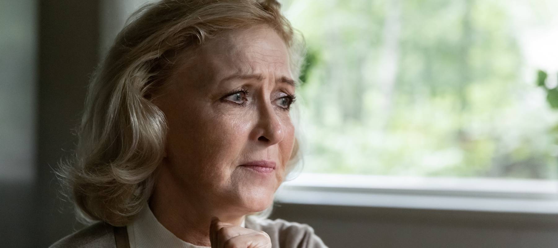 An older woman ponders by a window.
