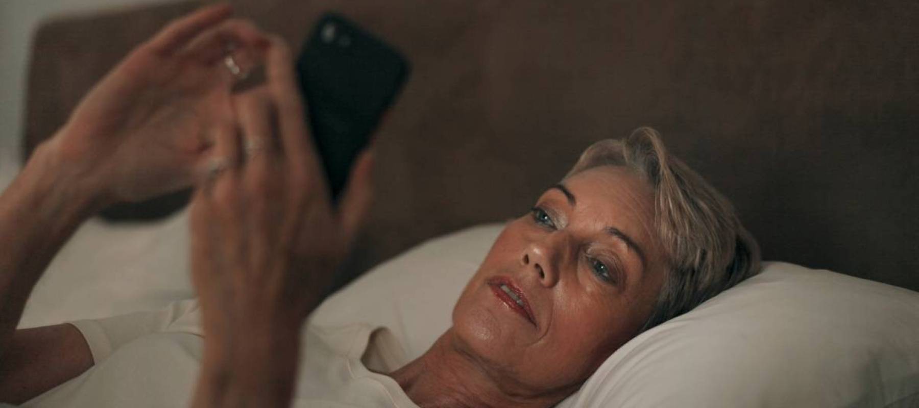 Older woman in bed looking on phone in bed