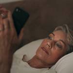 Older woman in bed looking on phone in bed