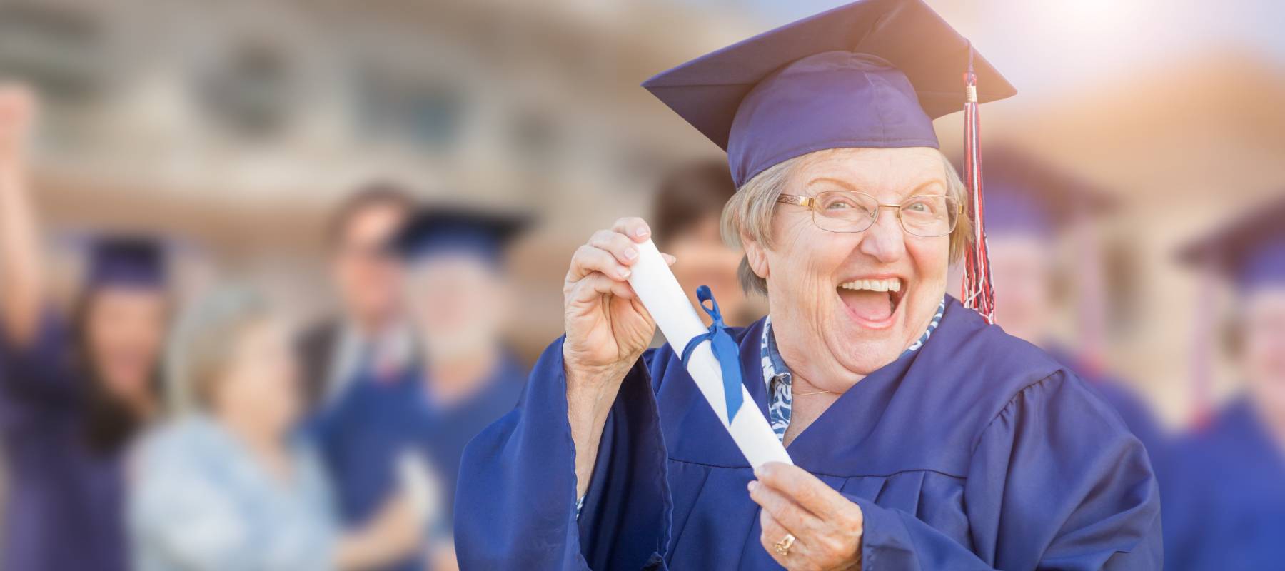 A happy older female in grad cap and gown, holding a rolled diploma.