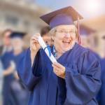 A happy older female in grad cap and gown, holding a rolled diploma.