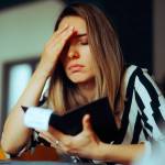 Unhappy young Caucasian woman looking at her check book