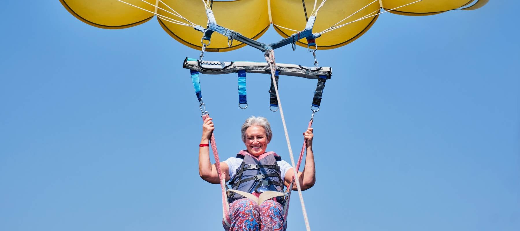 Woman with gray hair with a big smile and a fearless expression parasailing.