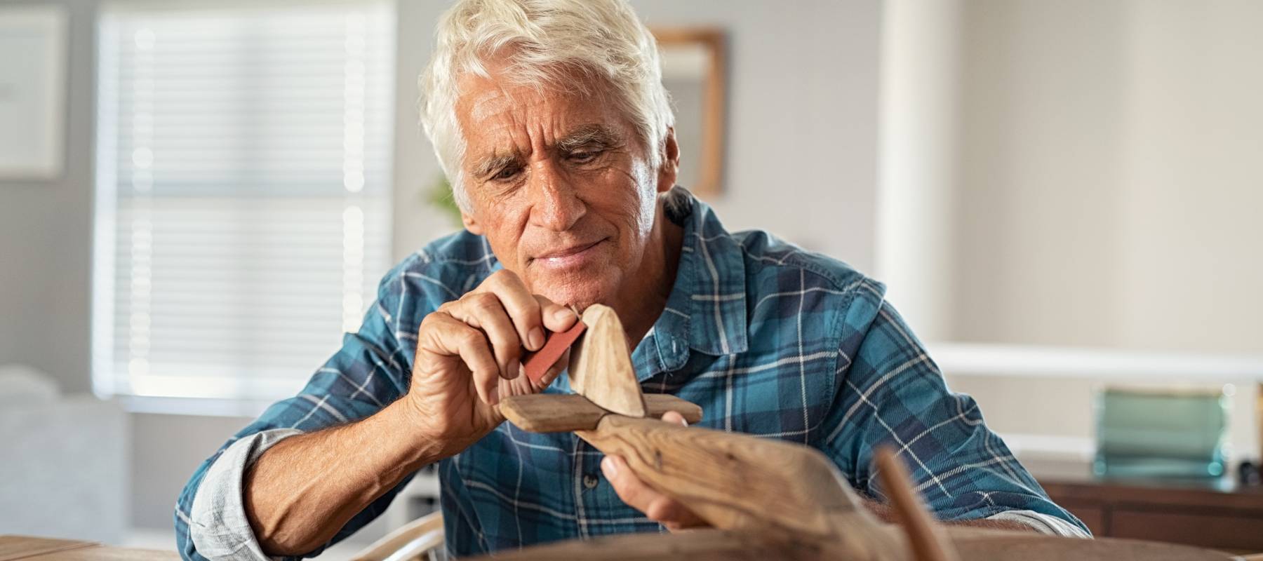 Retired man using sandpaper to polish wooden airplane sculpture.