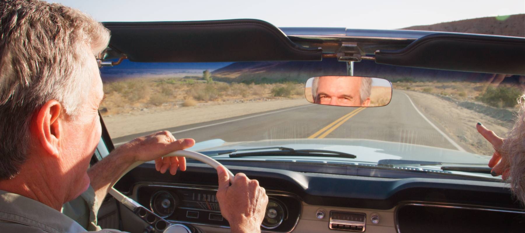 A couple driving a classic convertible along a country road.