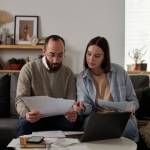 Busy middle-aged couple reviews and discusses their finances on a couch in a home setting.