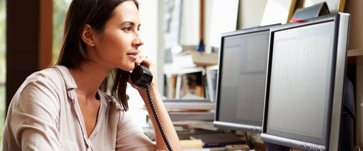 Woman on the phone in her home office, in front of the computer.