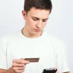 Portrait of a guy who holds a credit card and pays a mobile payment