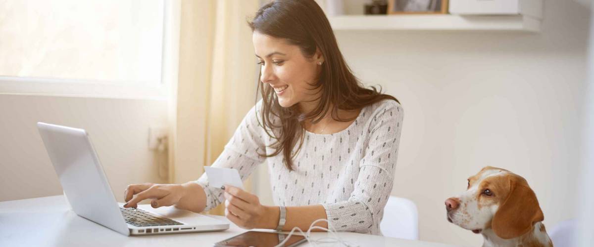 Young Caucasian businesswoman using credit card for on line payment. her dog next to her