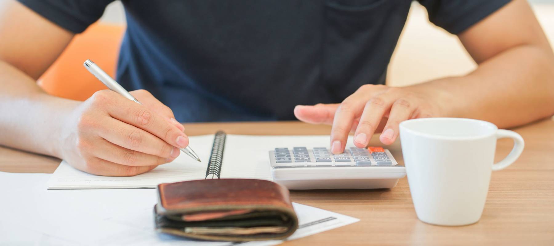 close up man hand writing on notebook and calculating on calculator about debt bills monthly at the table in home office and managing expense payroll,money risk financial concept