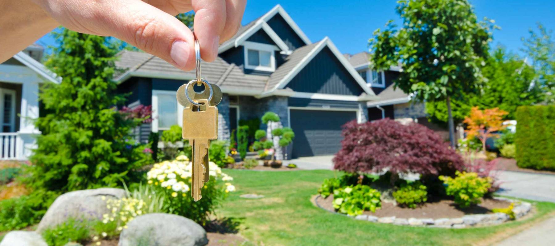 Hand holding the key to a brand new home, luxury house in the background.