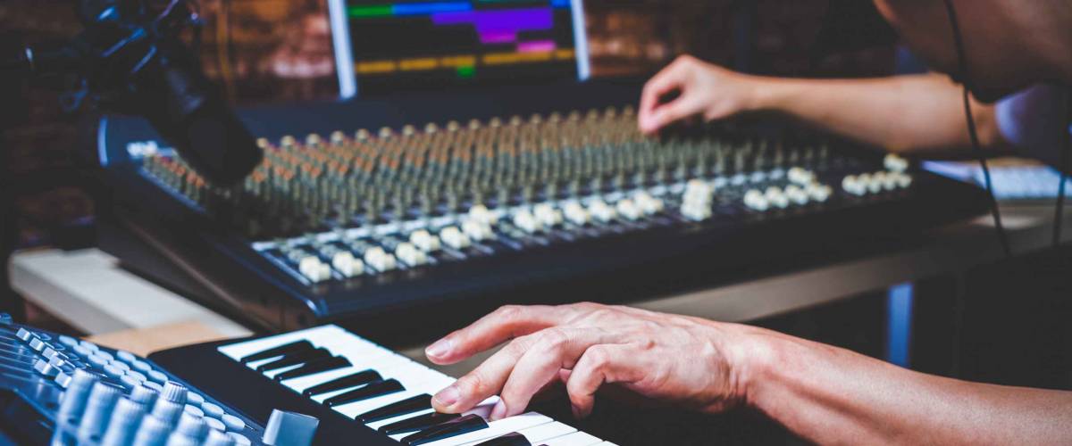 male musician playing midi keyboard synthesizer in recording studio