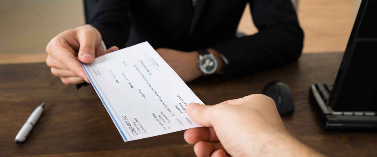 Close-up Of Businessman Hands Giving Cheque To Other Person In Office