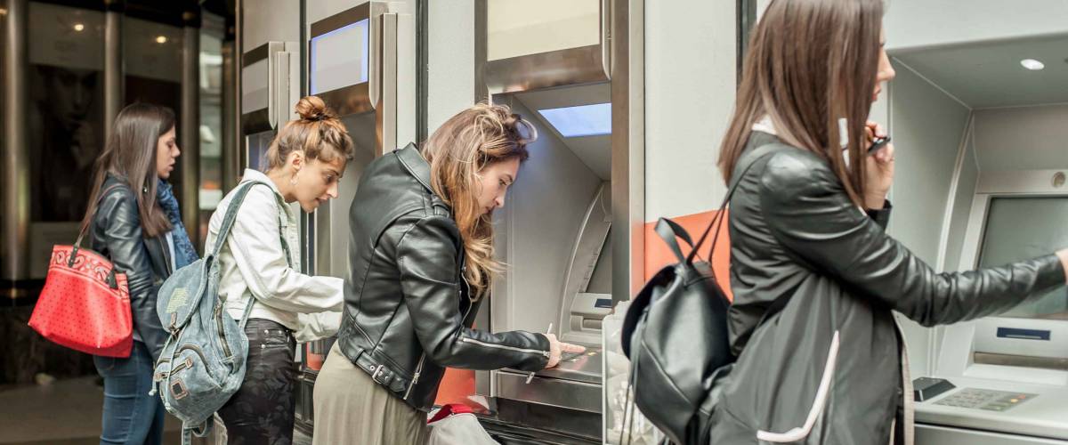 Four girl friends withdrawing money from credit card at ATM. Business woman