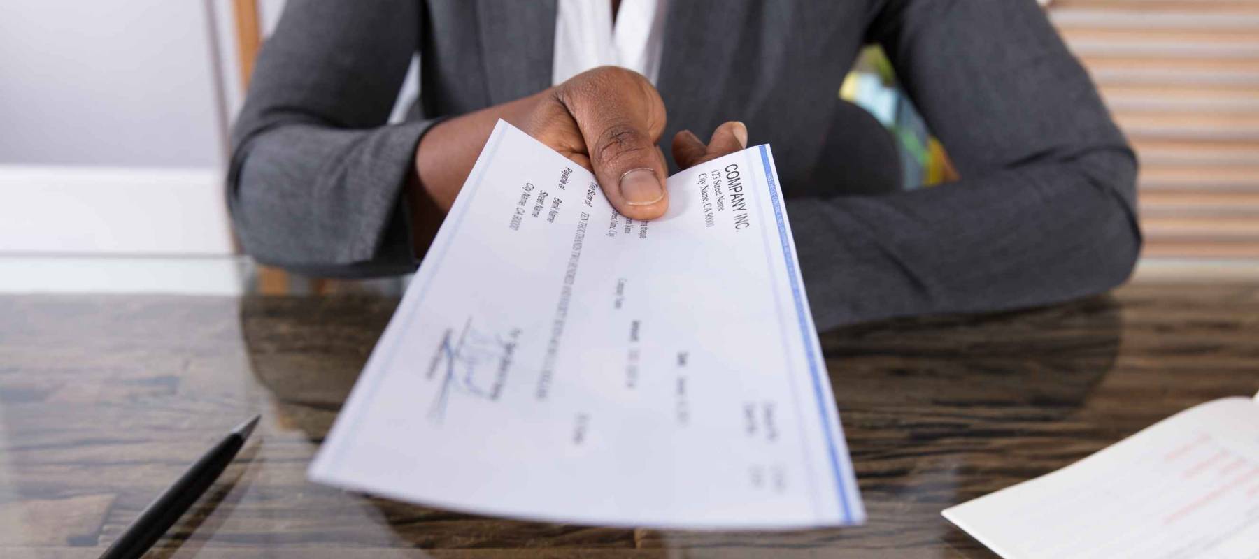 Close-up Of A Human Hand Giving Cheque On Desk