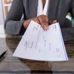 Close-up Of A Human Hand Giving Cheque On Desk