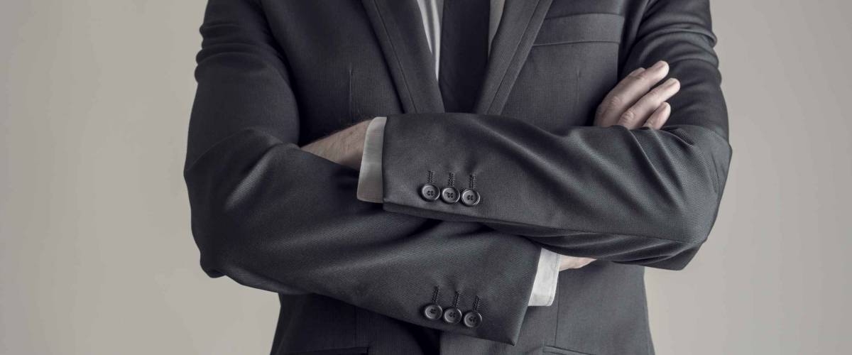 Torso of a businessman standing with folded arms in a classic black suit, vintage effect toned image.