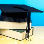 Coin in the jar with text RESP(Registered Education Savings Plan ), books and graduation hat on wooden background.