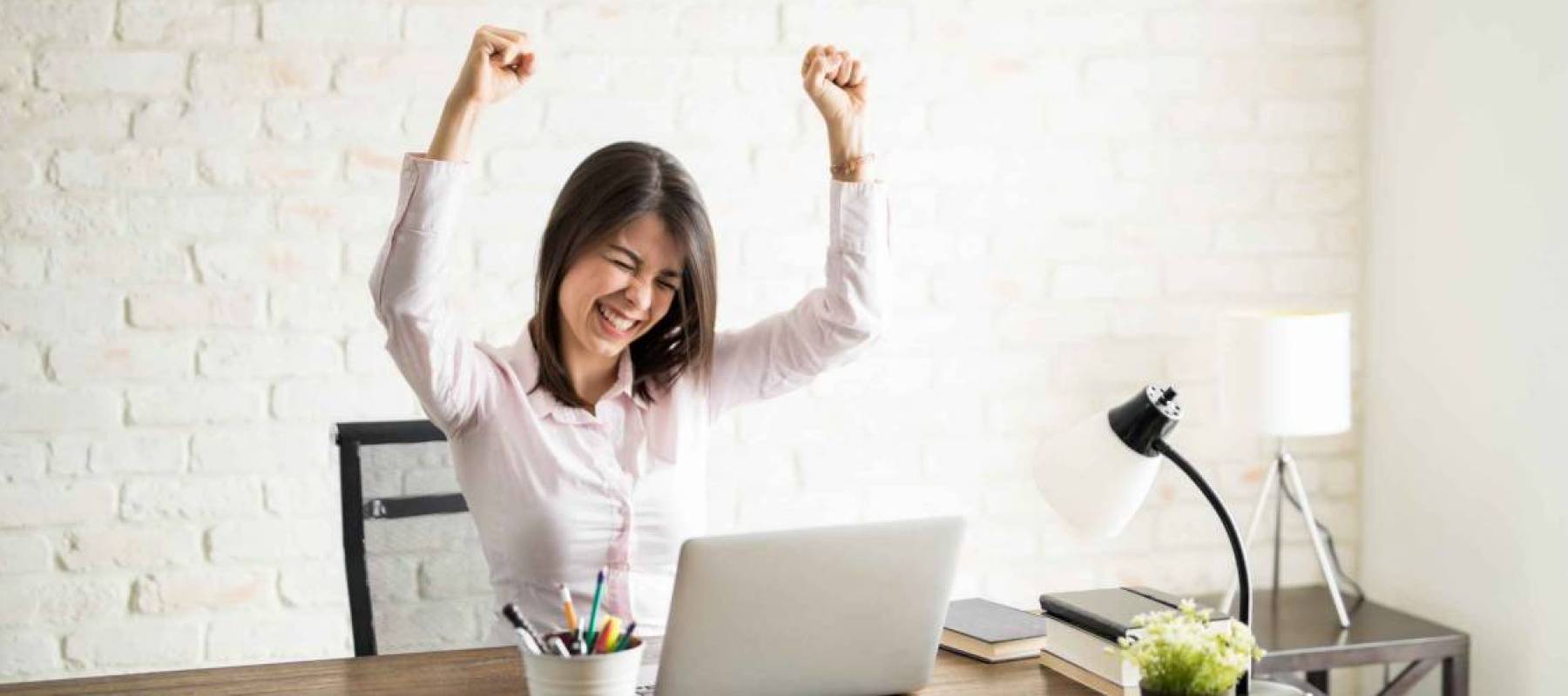 Excited woman using the computer and celebrating some good news with her arms up