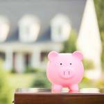 Piggy bank in front of a house, house is blurred, implying focus on savings over mortgage payoff.