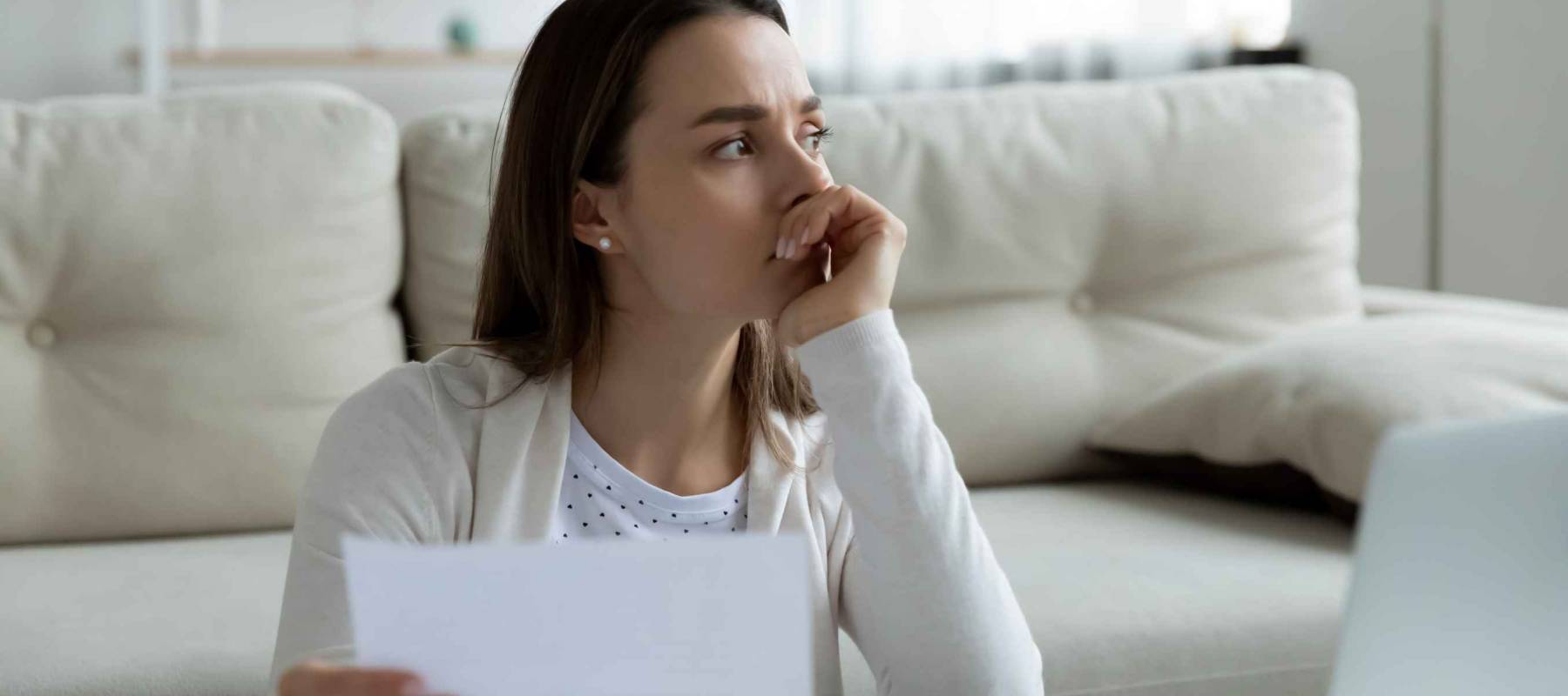 Thoughtful unhappy frustrated young woman holding paper letter with in front of computer
