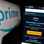 Person holding cellphone with webpage of subscription service Amazon Prime in front of business logo.