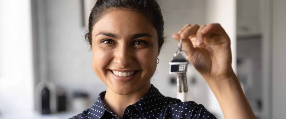 Close up portrait of smiling millennial Indian woman hold show keys to new house.