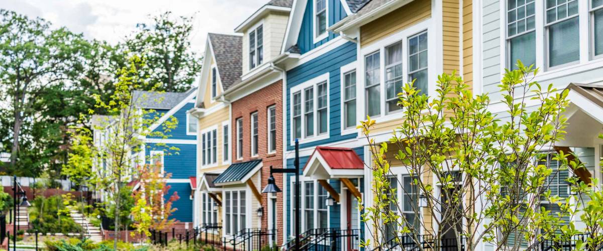 Row of colorful, red, yellow, blue, white, green painted residential townhouses, homes, houses with brick patio gardens in summer