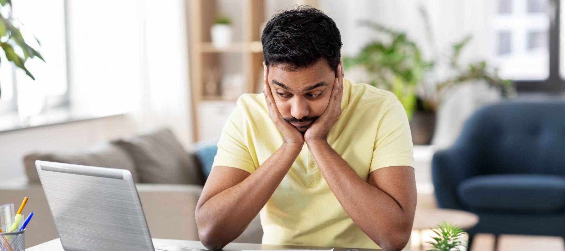 remote job, technology and people concept - unhappy young indian man with calculator and papers working at home office