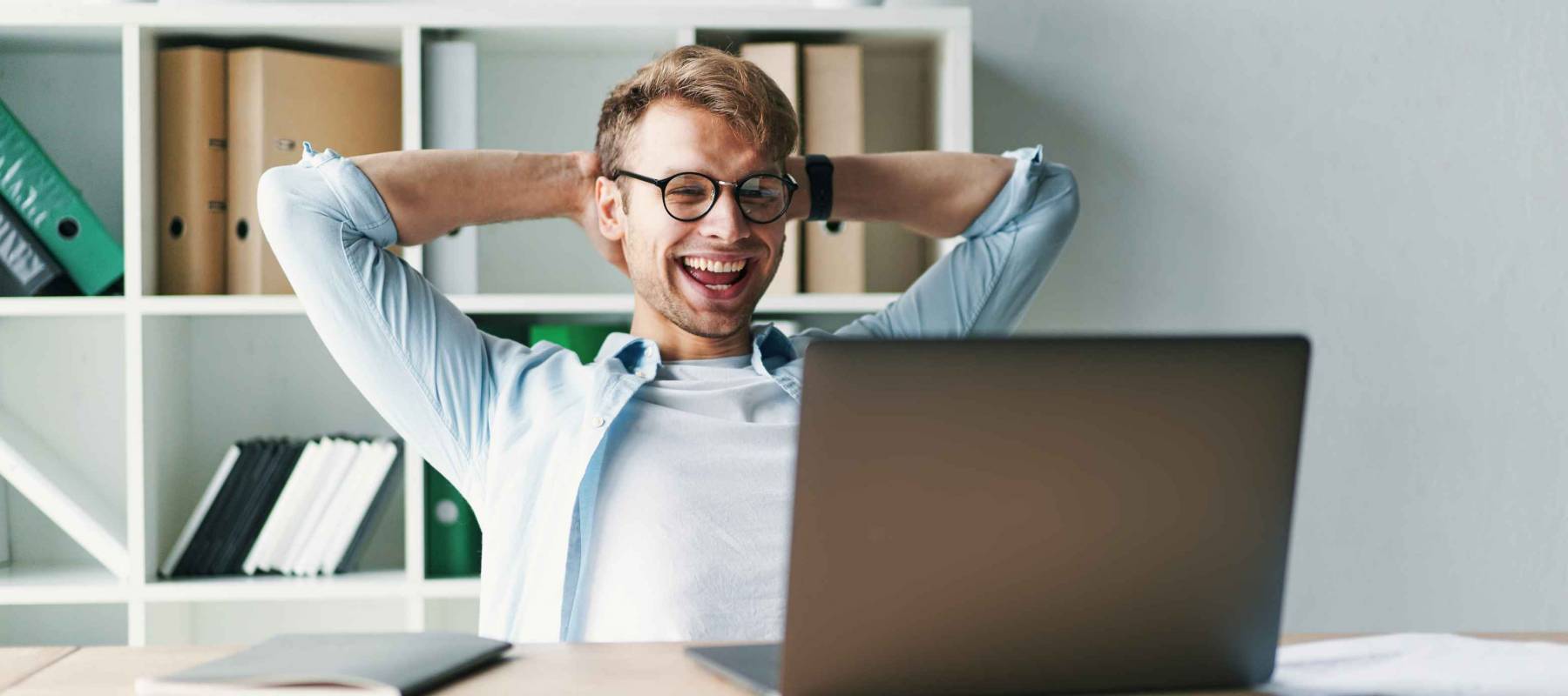 Young man smiling as he reads the screen of a laptop computer while relaxing working on a comfortable place by the wooden table at home. Happy Social distancing