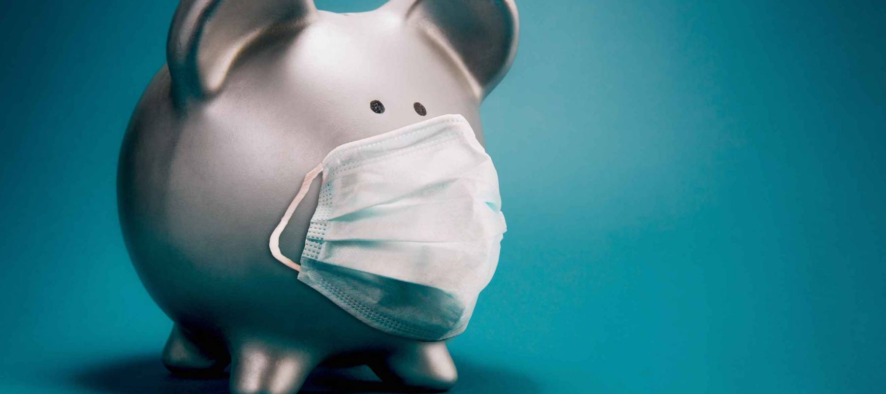Close up of piggy bank, wearing protective face mask, isolated on blue background. Money saving concept in time of coronavirus pandemic.