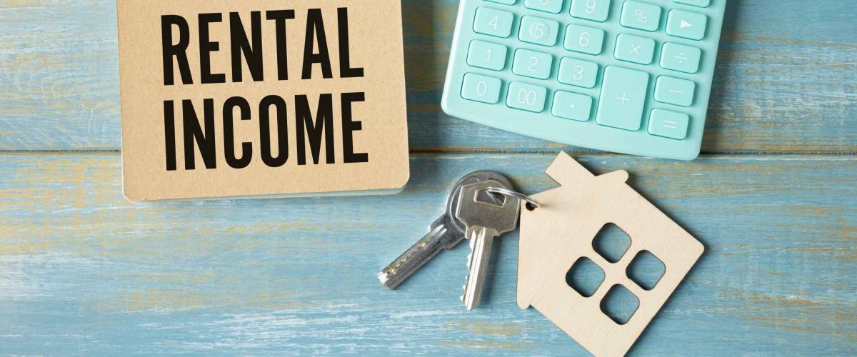 The word rental income is written in a notebook that sits on a gray desktop along with a laptop. Business image