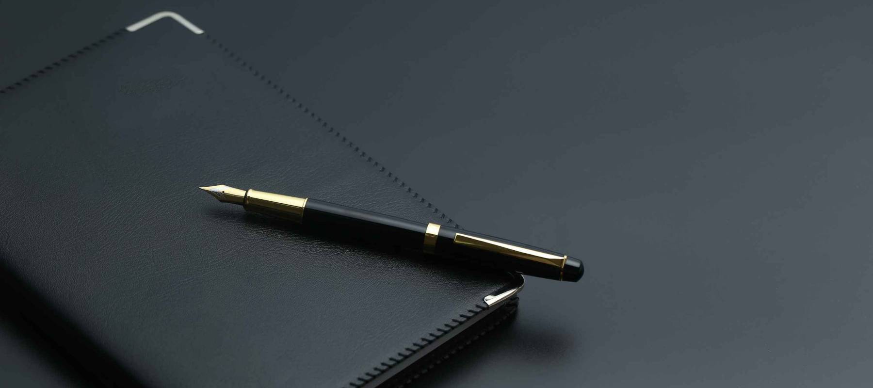 golden pen,notebook,calculator and glasses on black desk