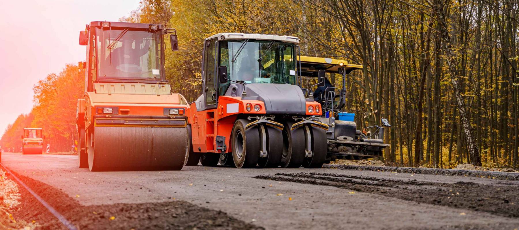 Two red special autos paving new asphalt driving in line one near another. New road construction. Selective focus.