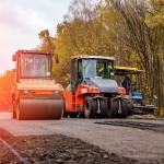 Two red special autos paving new asphalt driving in line one near another. New road construction. Selective focus.